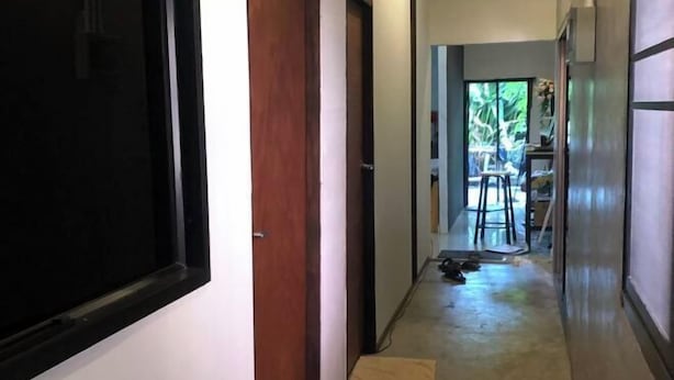 A narrow hallway with a wooden door on the left, a small rug on the floor, and a window at the end.