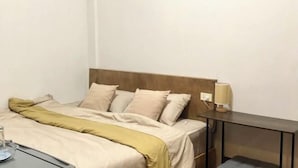 A neatly made bed with a wooden headboard, a bedside table with a lamp, and a small drawer unit.