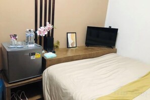 A hotel room with a bed, a desk with a TV, a small fridge, and a plant. - nine guesthouse (Chiang Rai)