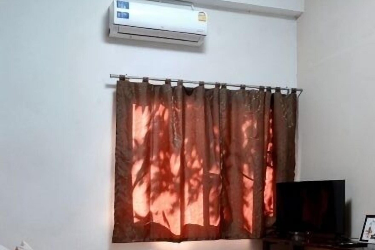 A bedroom with a bed, a bedside table, an air conditioner, a TV, and a curtain.