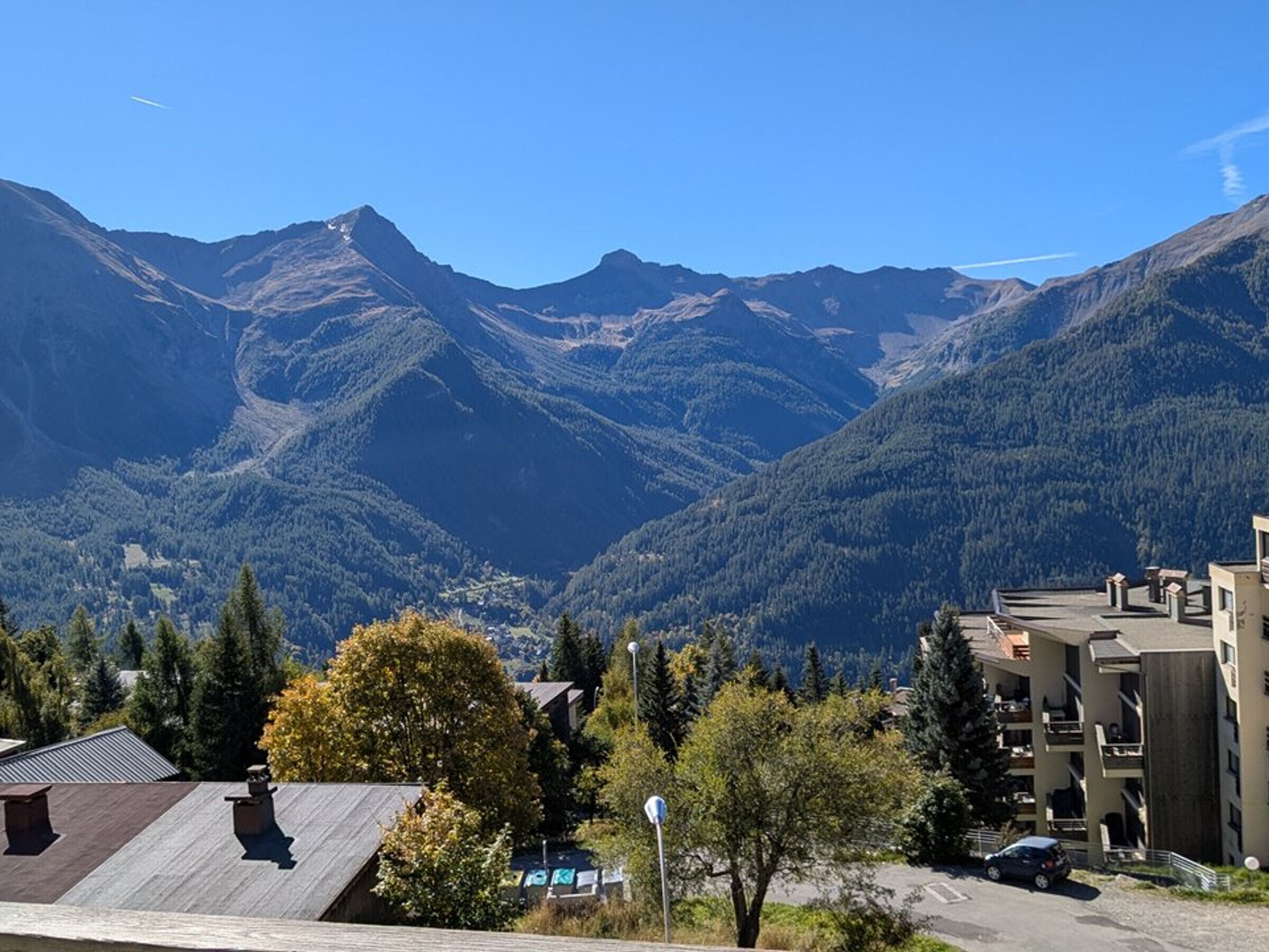 Zona residencial con montañas al fondo, que presenta un edificio de varios pisos con balcones y una estructura de techo plano en primer plano.