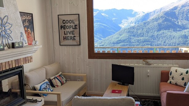 A cozy living room with a sofa, a small table with a TV, and a view of a mountainous landscape.