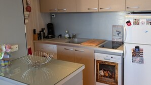 A compact kitchen with wooden cabinets, a dishwasher, a coffee maker, and a small refrigerator.