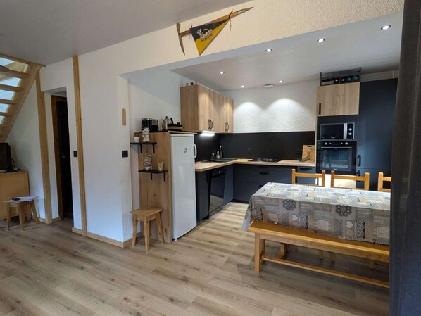 A compact kitchen with modern appliances, wooden cabinets, and a dining area with a patterned tablecloth.