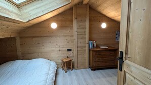 Un dormitorio acogedor en el ático con un tragaluz, paredes de madera, un pequeño aparador de madera y una cama.