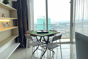Une pièce avec une table de billard, des chaises, une bibliothèque et une grande fenêtre donnant sur la ville.