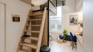 A loft bedroom with a wooden ladder, a desk, and a chair. - Kensington The Loft XL (London)
