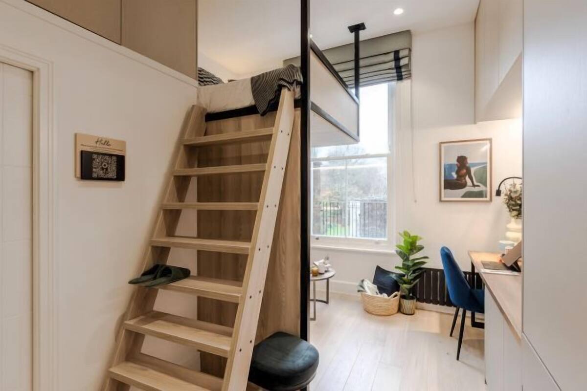 A loft bedroom with a wooden ladder, a desk, and a chair.