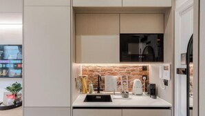 A modern kitchen with a built-in microwave, a coffee maker, and a kettle on the countertop. - Kensington The Loft XL (London)