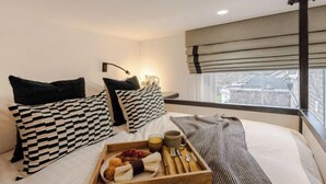 A hotel room with a bed, a tray with breakfast items, a window with a view, and a wall-mounted lamp. - Kensington The Loft XL (London)