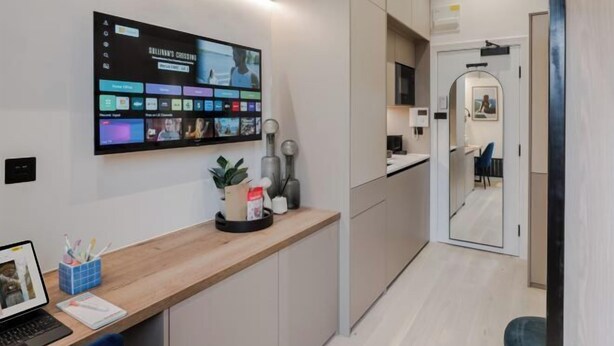 A modern kitchen with a large digital screen displaying various content, a wooden countertop, and a mirror reflecting the room. - Kensington The Loft XL (London)