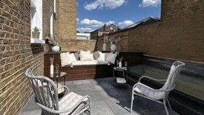 An outdoor patio with a sofa, two chairs, a small table, and a decorative vase. - B Comfort Apartments (London)