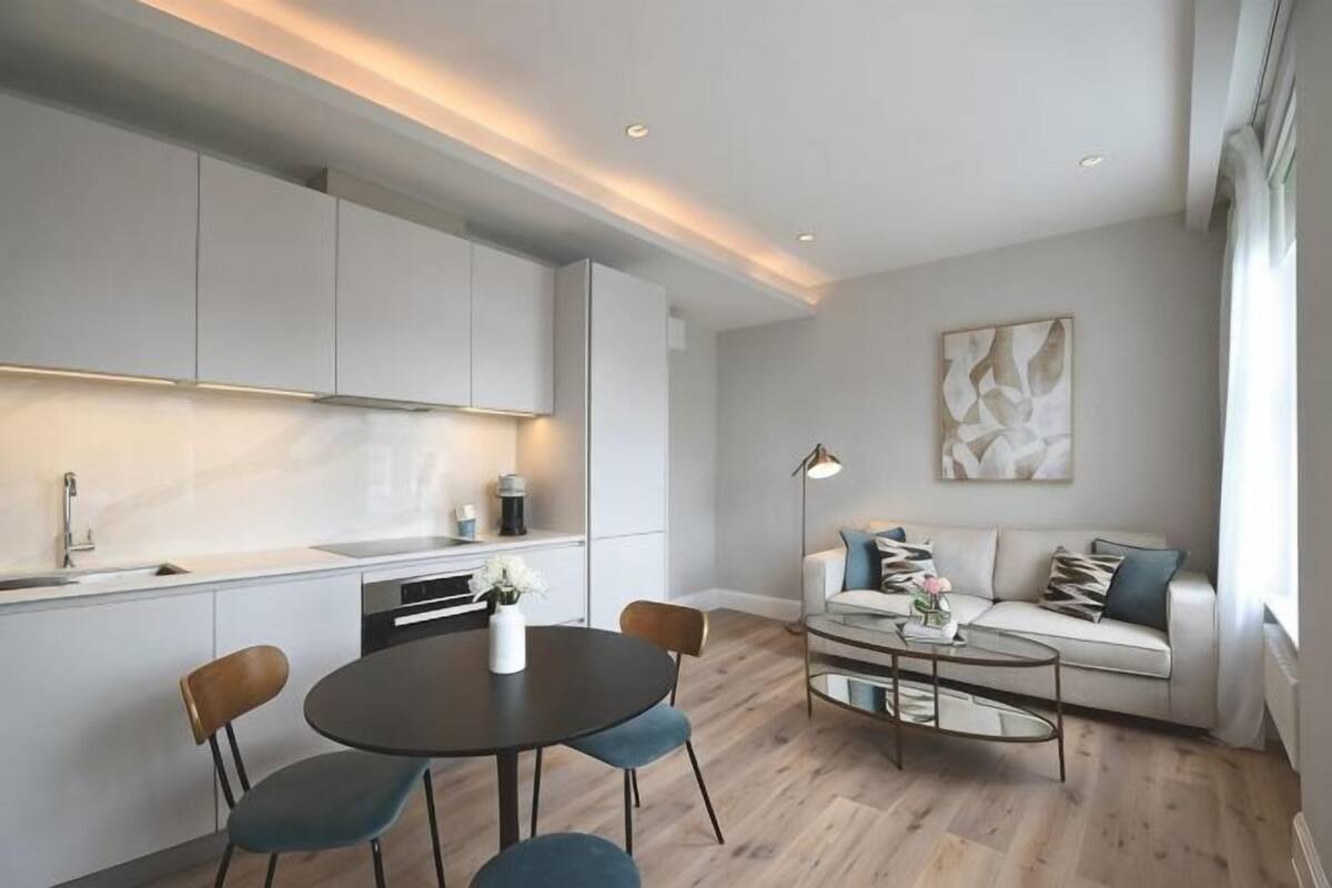 A modern kitchen with white cabinets, a dining area with a round table and chairs, and a living area with a sofa and coffee table.