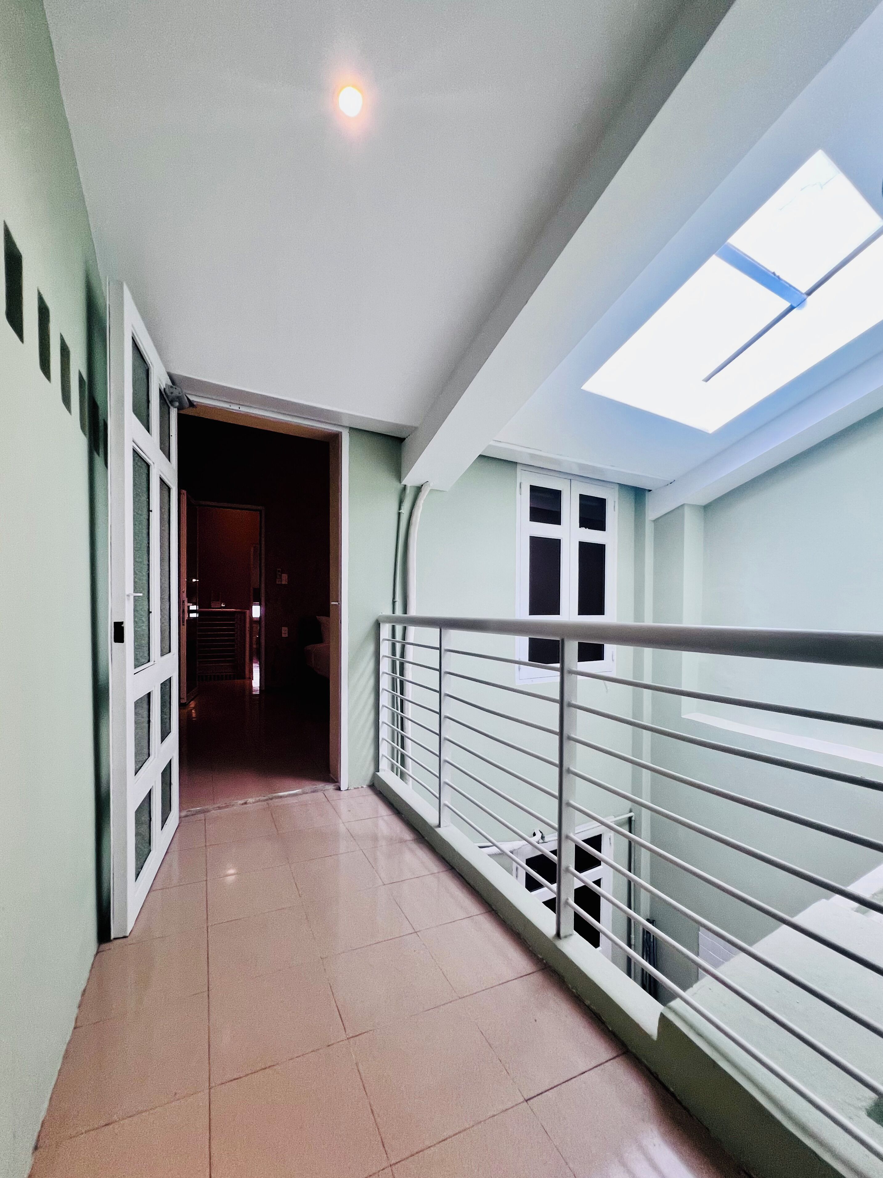Um corredor com claraboia, guarda-corpo de metal e piso ladrilhado.