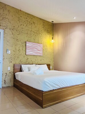Una cama bien hecha con sábanas blancas y una toalla enrollada, un cabecero de madera, una lámpara de pared y una pared con textura.