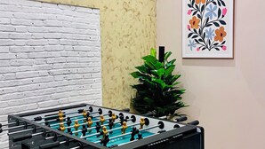 Una mesa de fútbol de mesa en una habitación con pared de ladrillo, una planta en maceta y una obra de arte floral enmarco.