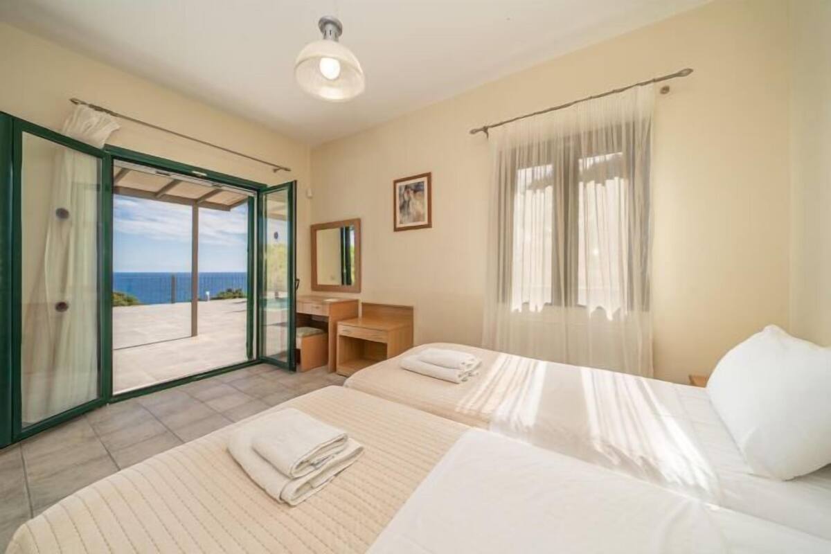 Habitació d'hotel amb dos llits, un bany i una porta corredissa de vidre que dona a un balcó amb vista al mar.