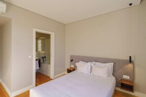 A bedroom with a bed, bedside tables, a nightstand, and a door leading to a bathroom. - N Apartments - Bolhão (Porto)