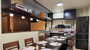 A modern kitchen with a dining table set for four, equipped with a microwave, stove, and refrigerator. - Shirahama no Kaze (Shirahama)