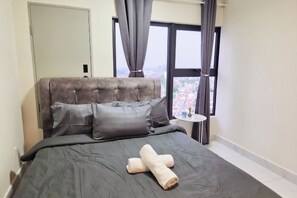 Een slaapkamer met een groot bed, grijze beddengoed, een raam met gordijnen en uitzicht op een stadsgezicht.