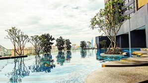 Une piscine à débordement située sur le toit, avec un sol carrelé, entourée d’arbres et d’un bâtiment moderne.