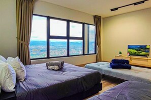 Een hotelkamer met twee bedden, een groot raam met uitzicht op de stad, een televisie en een klein tafeltje.