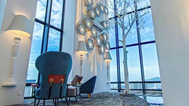 Un intérieur moderne avec de grandes fenêtres, un luminaire aux formes géométriques et une sculpture en forme d’arbre.