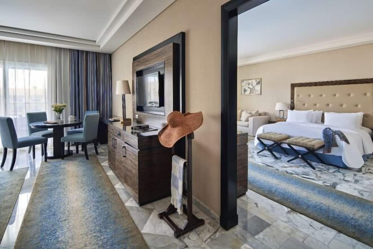 A hotel room with a bed, a desk, a chair, a TV, and a coat rack.