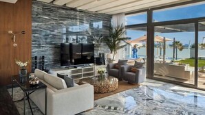 A modern living room with a large TV, comfortable seating, a marble floor, and a view of the sea. - Ghazala Luxury Collection Alamein (Qesm Ad Dabaah)