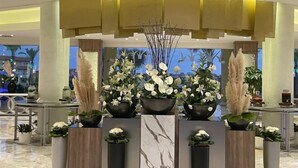A lobby with a central floral arrangement, marble columns, and a modern ceiling design. - Ghazala Luxury Collection Alamein (Qesm Ad Dabaah)