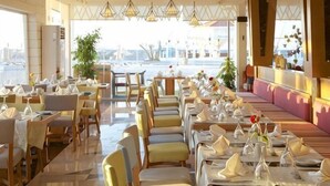 A restaurant with tables set for dining, large windows, and hanging light fixtures. - Ghazala Luxury Collection Alamein (Qesm Ad Dabaah)
