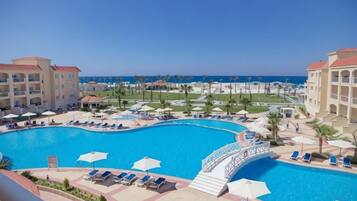 A resort pool area with a bridge, lounge chairs, umbrellas, and a view of the ocean.