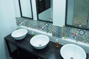 Ein Badezimmer mit drei weißen Waschbecken, einer dunklen Arbeitsplatte und einer gefliesten Rückwand.