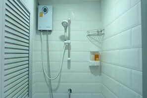 Una ducha con cabezal de ducha de mano, panel de control en la pared y un estante pequeño con artículos de aseo.