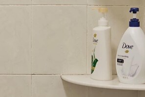 Zwei Dove Pflegeprodukte auf einem weißen Regal vor einer gefliesten Wand.