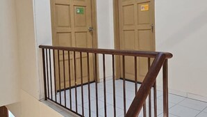 Un escalier avec une main courante en bois et une rampe en métal, menant à une pièce dotée de deux portes beiges, chacune ornée d’une petite plaque.