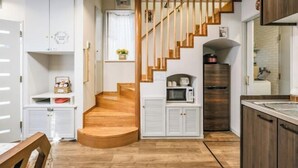 Une cuisine avec un plancher en bois, des meubles blancs, un escalier en bois et un four à micro-ondes posé sur le comptoir.