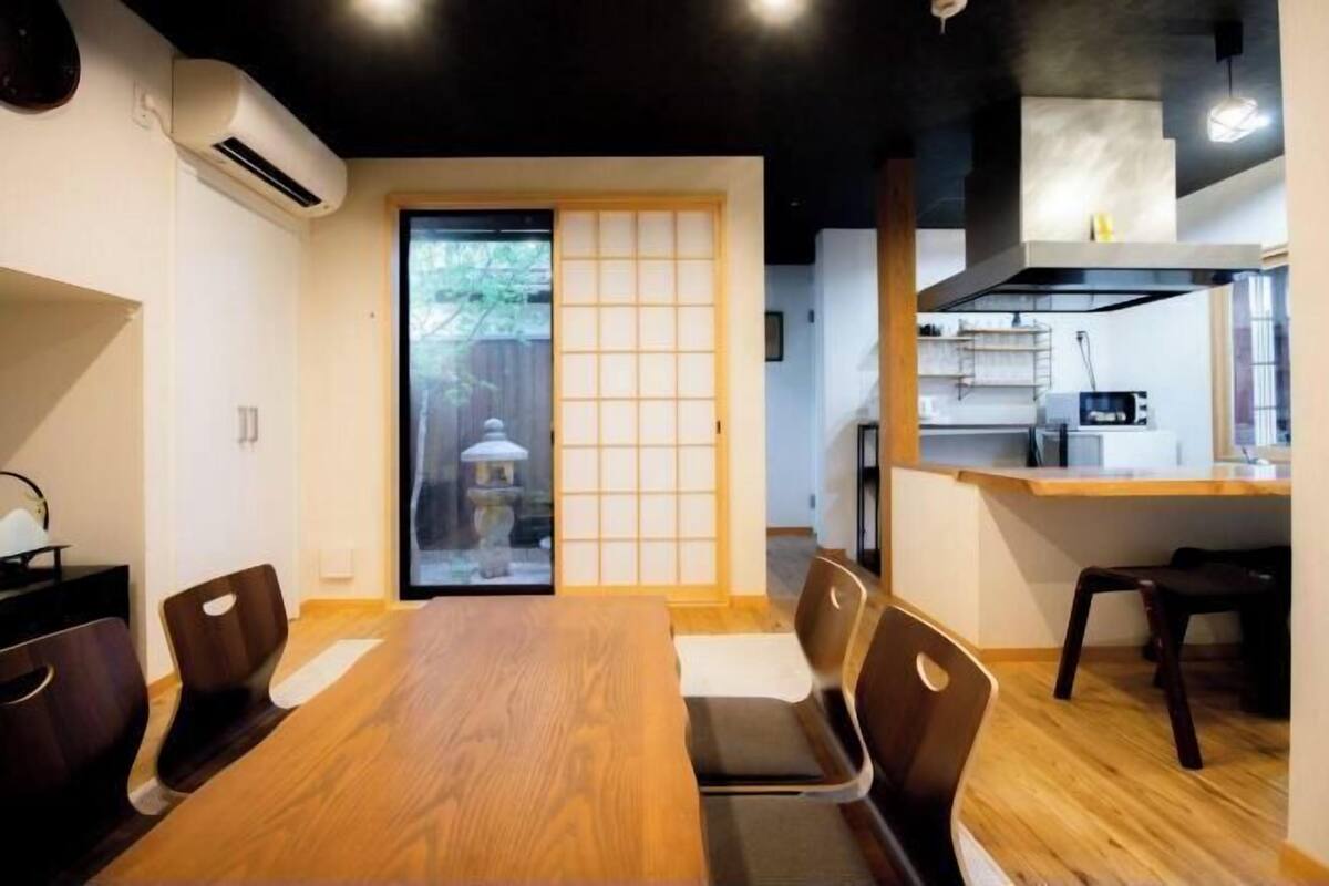 Un comedor con una mesa y sillas de madera, una puerta corredera con vistas y una cocina al fondo.