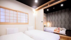 A hotel room with two beds, a sliding shoji screen, a dark textured wall, and a nightstand with a lamp. - Kyoya Nobuhiro Reisen (Kyoto)