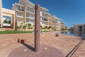 A pool area with a tiled floor, a central column, and a building with balconies in the background. - BnB Homes Ocean View Apartment with relax Terrace, 2 Swimming pools & Tennis court (Albufeira)