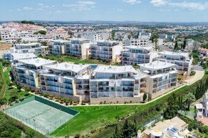 A modern residential complex with multiple apartment buildings, a tennis court, and a landscaped area. - BnB Homes Ocean View Apartment with relax Terrace, 2 Swimming pools & Tennis court (Albufeira)