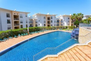 A swimming pool surrounded by lounge chairs and a building with balconies. - BnB Homes Ocean View Apartment with relax Terrace, 2 Swimming pools & Tennis court (Albufeira)