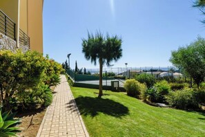 A paved pathway leading to a well-maintained lawn with a palm tree, surrounded by various shrubs and plants. - BnB Homes Ocean View Apartment with relax Terrace, 2 Swimming pools & Tennis court (Albufeira)