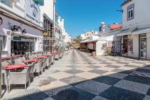 A cobblestone street with outdoor seating, buildings with signage, and a clear blue sky. - BnB Homes Ocean View Apartment with relax Terrace, 2 Swimming pools & Tennis court (Albufeira)