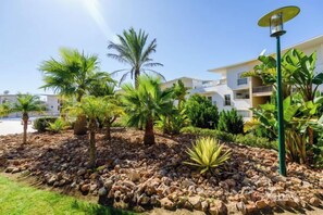 A landscaped garden with palm trees and a street lamp, surrounded by a building with multiple balconies. - BnB Homes Ocean View Apartment with relax Terrace, 2 Swimming pools & Tennis court (Albufeira)