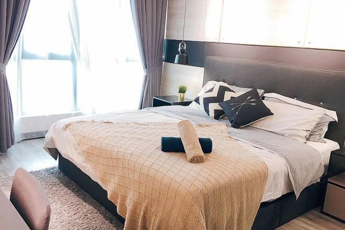 A modern bedroom with a large bed, a nightstand, a small plant, and a view of the outdoors.