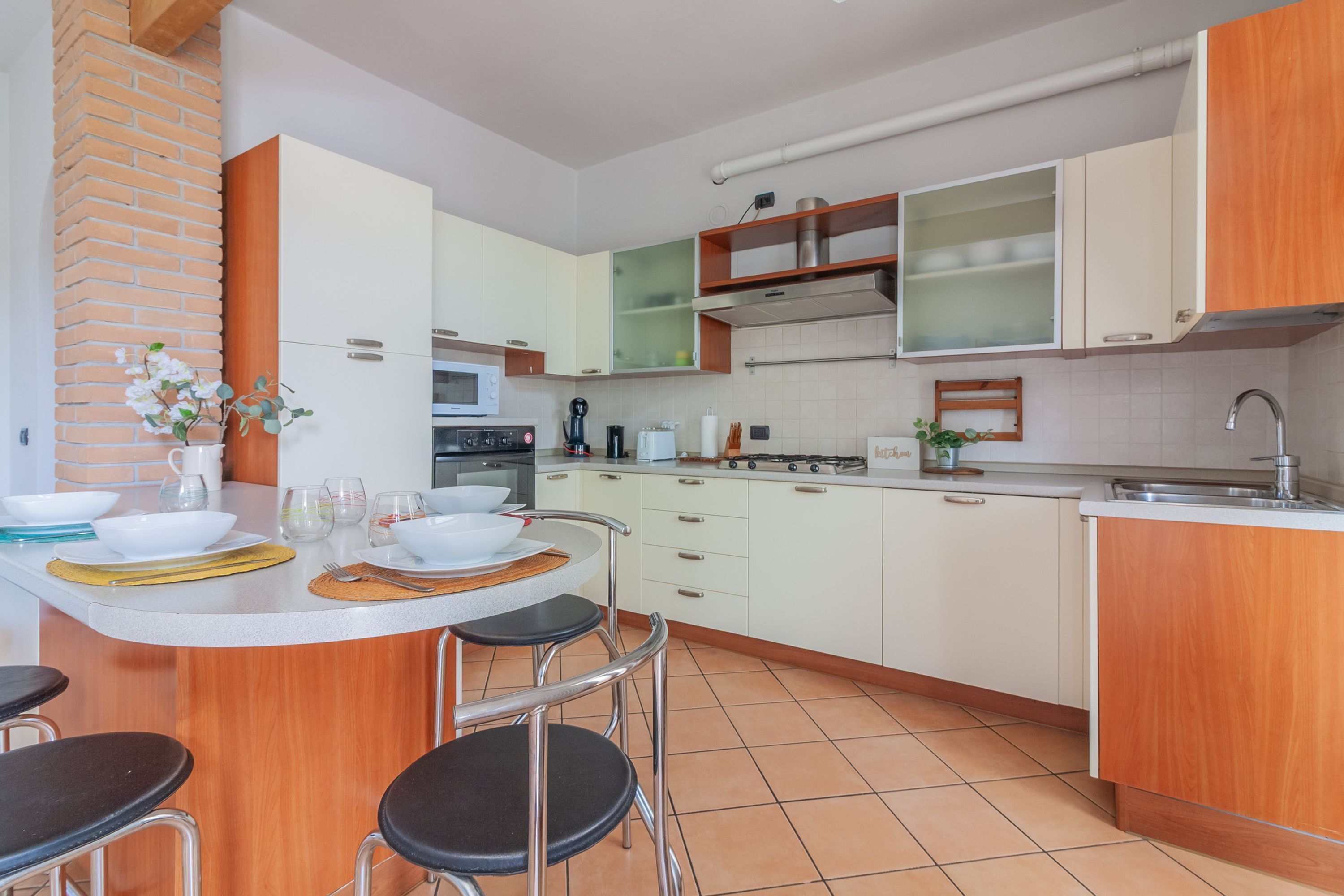 A compact kitchen with white cabinets, a brick wall, a wooden countertop, and a small dining area with stools.