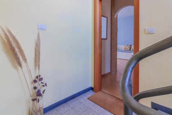 Un pasillo con una escalera, un interruptor de luz en la pared y una planta decorativa.