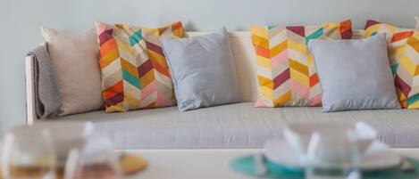 Una sala de estar moderna con un sofá decorado con almohadones de colores, una mesa de centro blanca y un posavasos color turquesa.