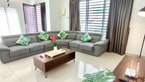 A modern living room with a grey sectional sofa, a wooden coffee table, and a large green plant. - Tropical Livings Meru Ipoh Homestay (Ipoh)